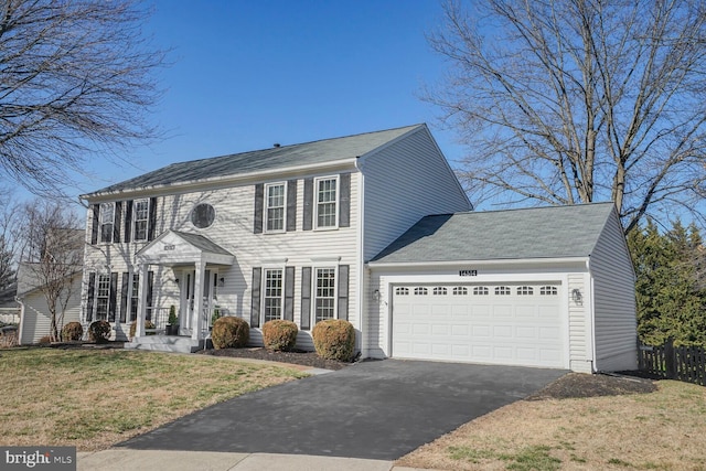 colonial-style house with a garage, driveway, a front lawn, and fence