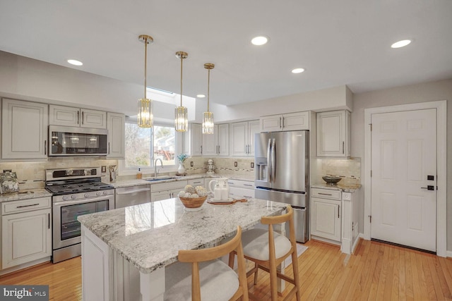 kitchen featuring stainless steel appliances, light stone counters, light wood-type flooring, and a sink