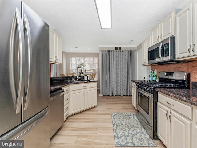 kitchen featuring stainless steel appliances, a sink, light wood-style floors, ornamental molding, and tasteful backsplash