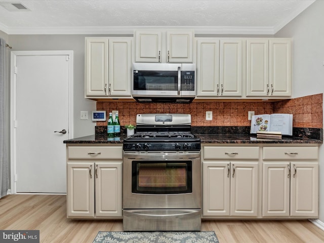 kitchen with visible vents, appliances with stainless steel finishes, ornamental molding, light wood finished floors, and tasteful backsplash