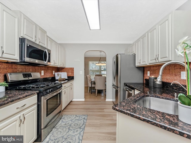 kitchen featuring arched walkways, stainless steel appliances, a sink, light wood-type flooring, and dark stone countertops