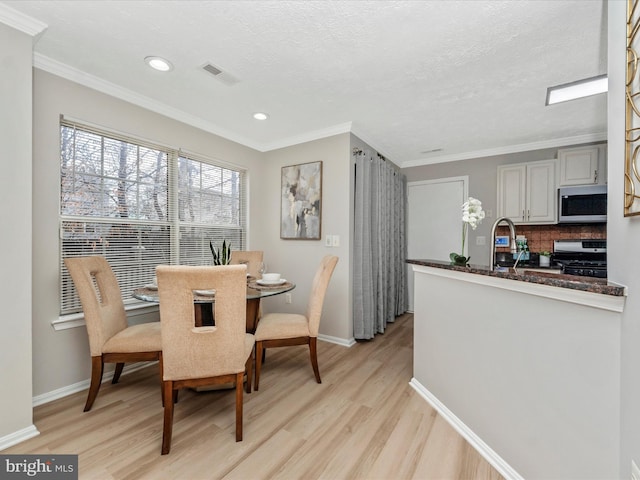 dining space with light wood-type flooring, visible vents, and crown molding