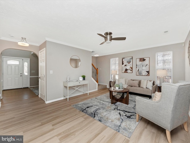 living area with arched walkways, crown molding, light wood-style flooring, baseboards, and stairs