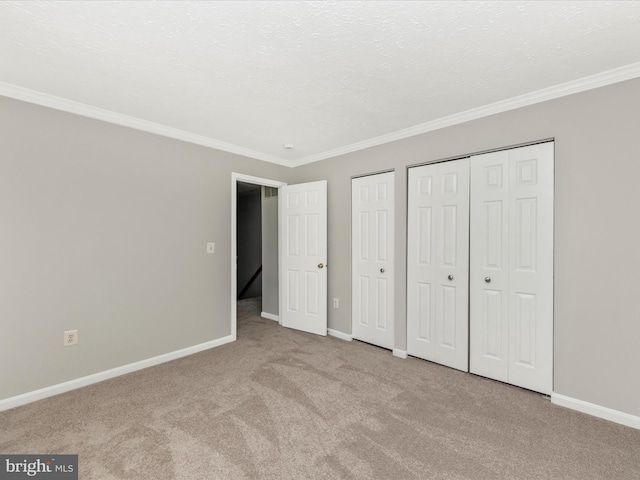 unfurnished bedroom with ornamental molding, carpet flooring, baseboards, and two closets