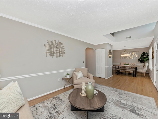 living area with arched walkways, a textured ceiling, wood finished floors, visible vents, and baseboards