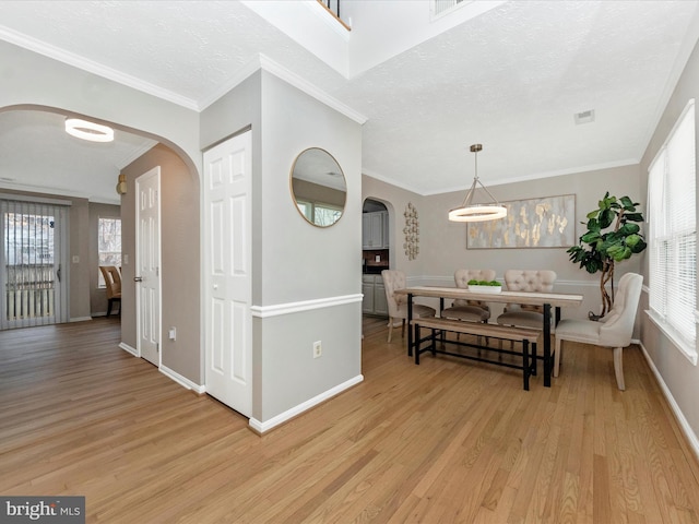 dining area featuring light wood-type flooring, arched walkways, and crown molding