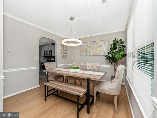 dining space with baseboards, visible vents, arched walkways, crown molding, and light wood-type flooring