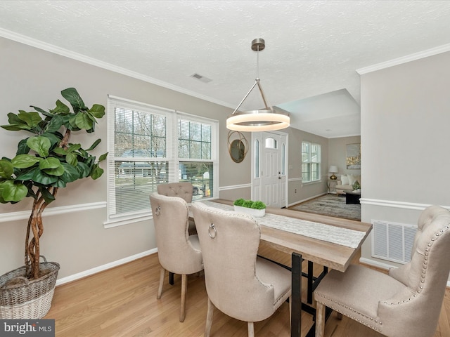 dining space featuring a textured ceiling, visible vents, baseboards, light wood finished floors, and crown molding