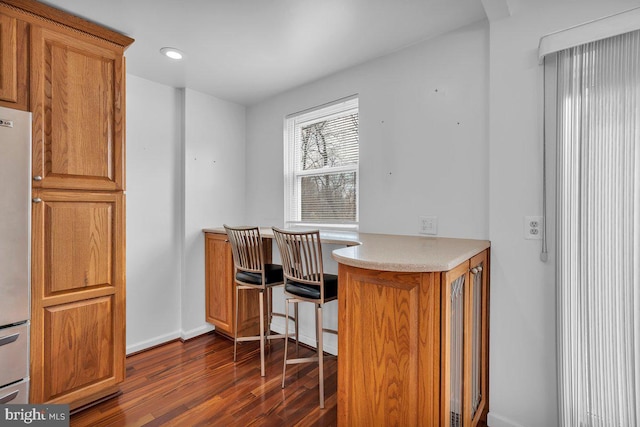 interior space with dark wood-type flooring, freestanding refrigerator, and brown cabinets