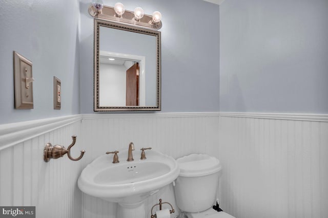 half bathroom with wainscoting, a sink, and toilet