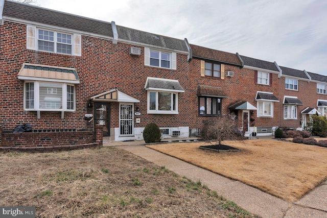 townhome / multi-family property with brick siding, a front lawn, a shingled roof, and mansard roof