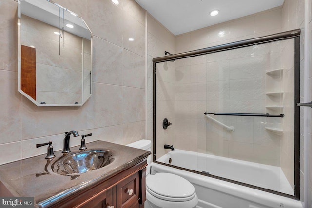 bathroom featuring toilet, enclosed tub / shower combo, tile walls, and vanity