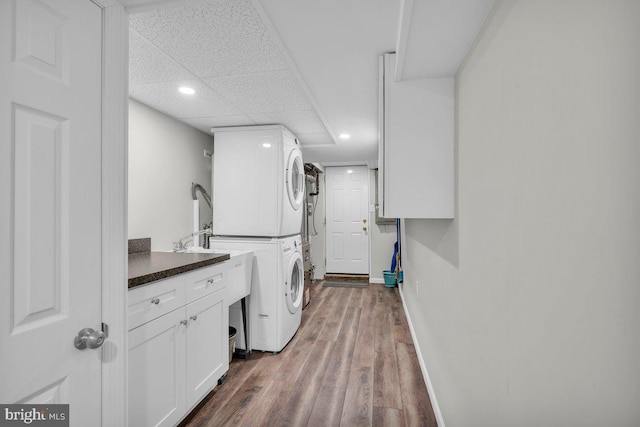 laundry room featuring cabinet space, baseboards, dark wood finished floors, stacked washer / dryer, and recessed lighting