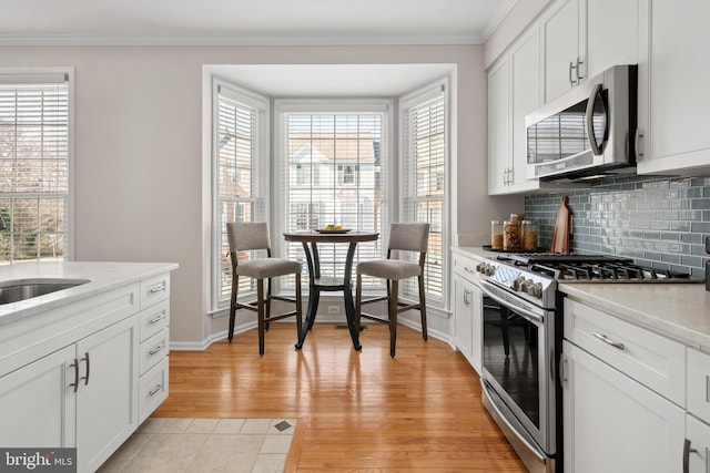 kitchen featuring ornamental molding, decorative backsplash, light wood-style floors, stainless steel appliances, and a sink