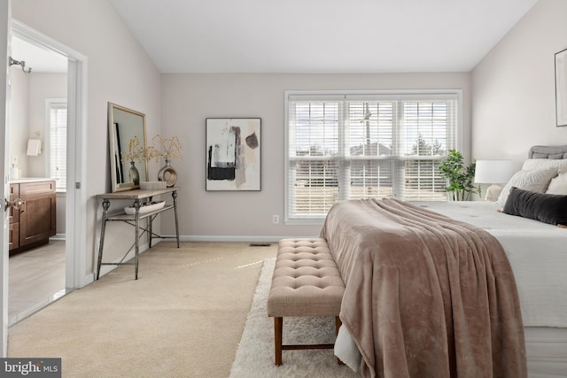 bedroom with visible vents, lofted ceiling, ensuite bathroom, baseboards, and light colored carpet