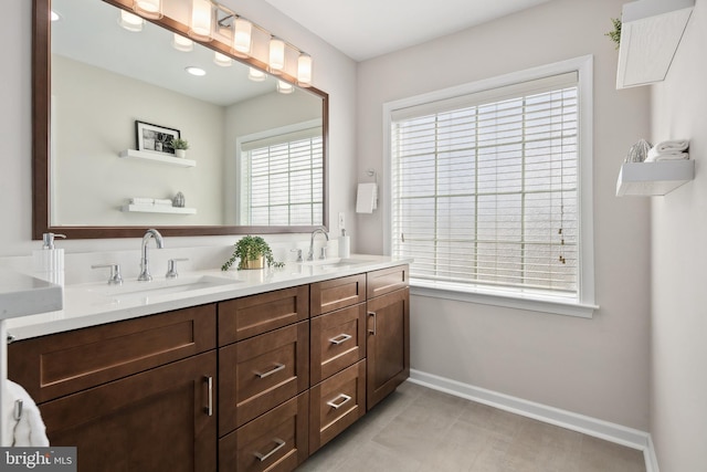 full bath featuring double vanity, baseboards, and a sink