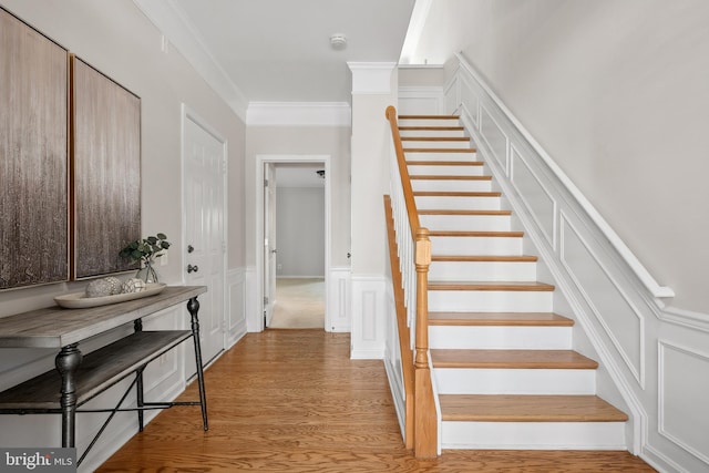 staircase with a decorative wall, wood finished floors, and ornamental molding