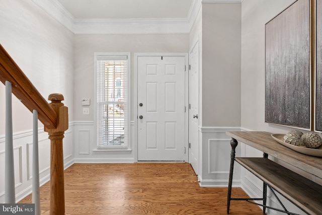 entrance foyer featuring crown molding, stairs, wainscoting, wood finished floors, and a decorative wall