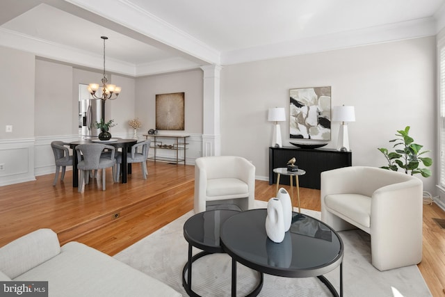 living area with light wood finished floors, a notable chandelier, ornamental molding, a decorative wall, and ornate columns