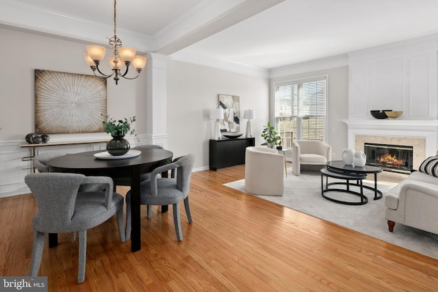 dining room featuring a notable chandelier, light wood-style flooring, ornamental molding, and a premium fireplace