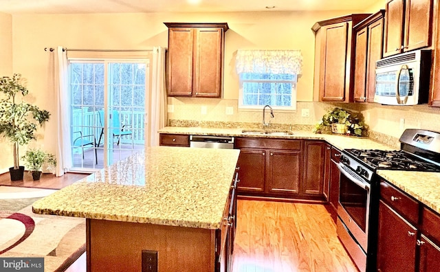 kitchen featuring appliances with stainless steel finishes, light stone countertops, light wood-style floors, and a sink