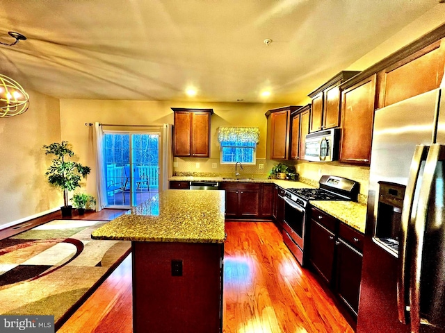 kitchen with a sink, light stone counters, appliances with stainless steel finishes, plenty of natural light, and wood-type flooring