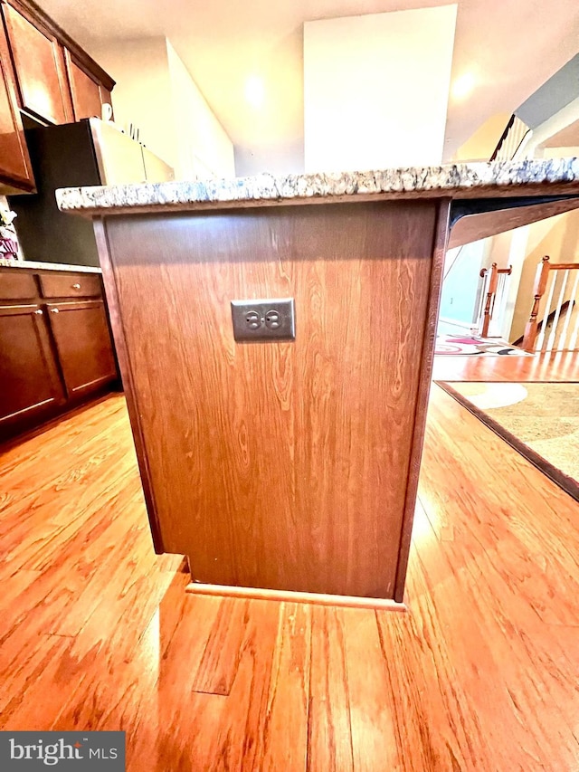 interior details featuring brown cabinets, light wood-type flooring, and light stone countertops