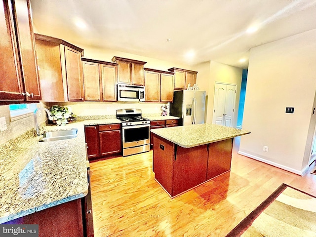 kitchen with a sink, a center island, stainless steel appliances, light wood-style floors, and baseboards