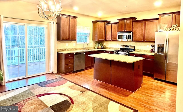 kitchen featuring a sink, decorative light fixtures, a kitchen island, light wood-style floors, and appliances with stainless steel finishes