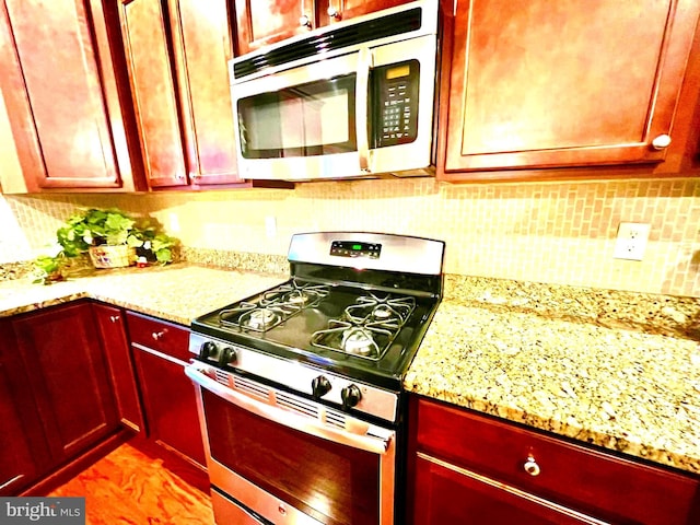 kitchen with stainless steel gas stove, tasteful backsplash, dark brown cabinets, and light stone countertops