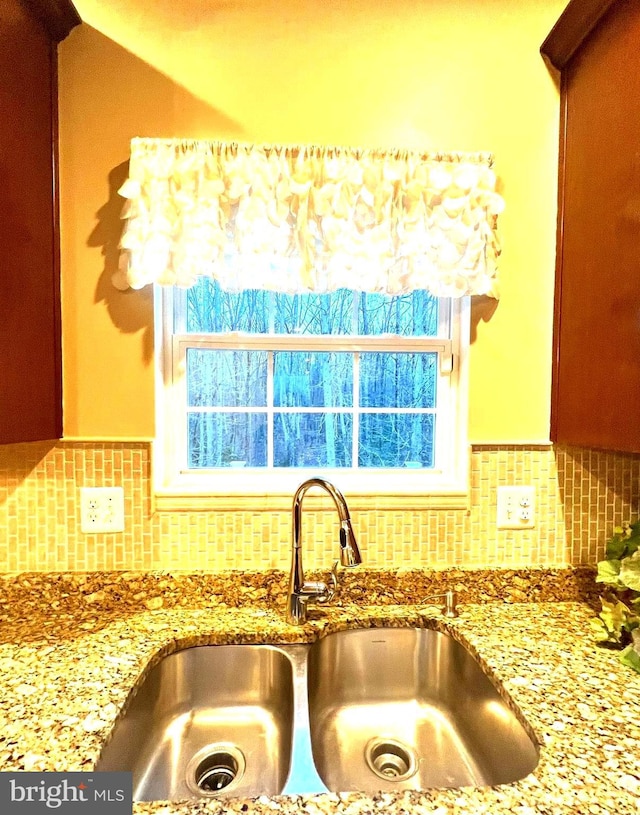 interior details featuring a sink, decorative backsplash, and light stone counters