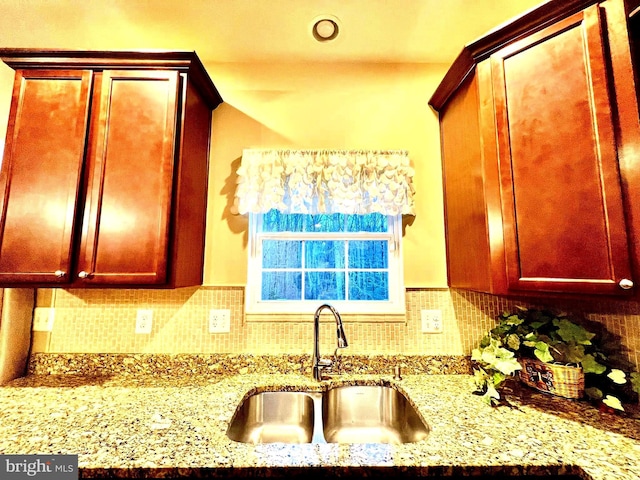 kitchen featuring light stone counters, decorative backsplash, reddish brown cabinets, and a sink