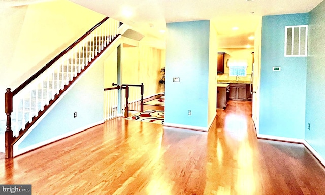 unfurnished living room with visible vents, baseboards, wood finished floors, and stairway