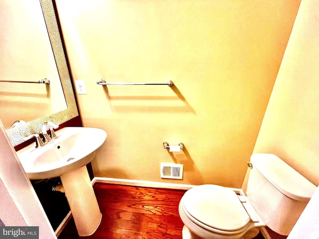 half bathroom with visible vents, toilet, baseboards, and wood finished floors