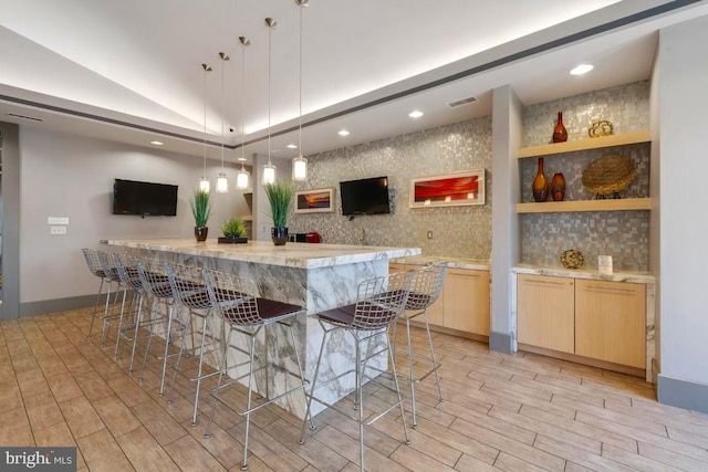 kitchen with visible vents, light brown cabinetry, a breakfast bar area, wood tiled floor, and vaulted ceiling