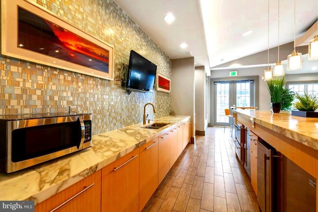 kitchen with pendant lighting, a sink, stainless steel microwave, backsplash, and wood finished floors