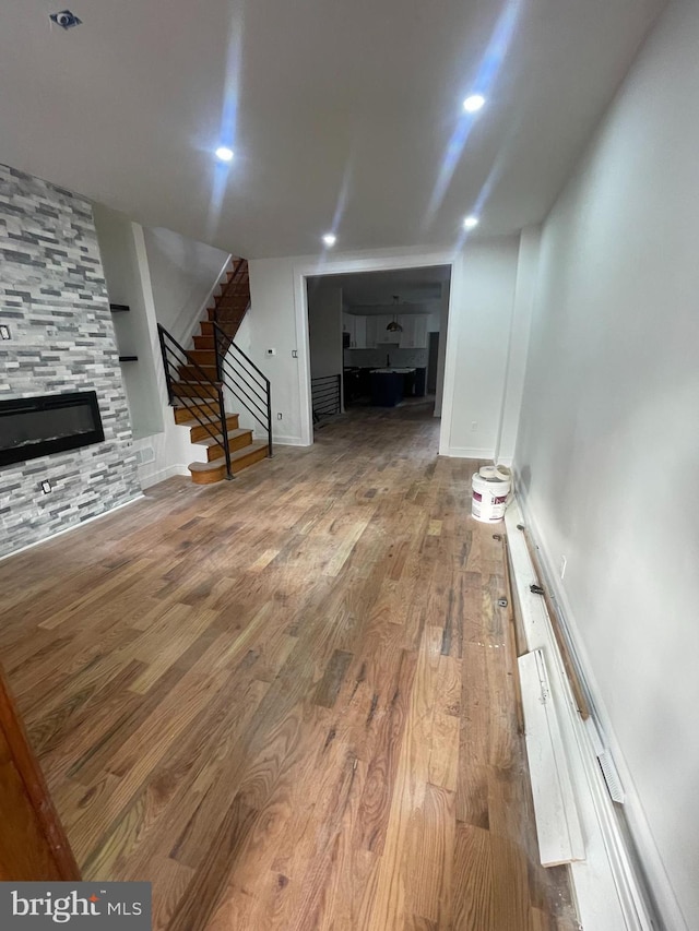 unfurnished living room featuring a fireplace, recessed lighting, wood finished floors, baseboards, and stairs