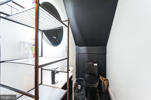 washroom featuring baseboards, marble finish floor, and stacked washer and clothes dryer