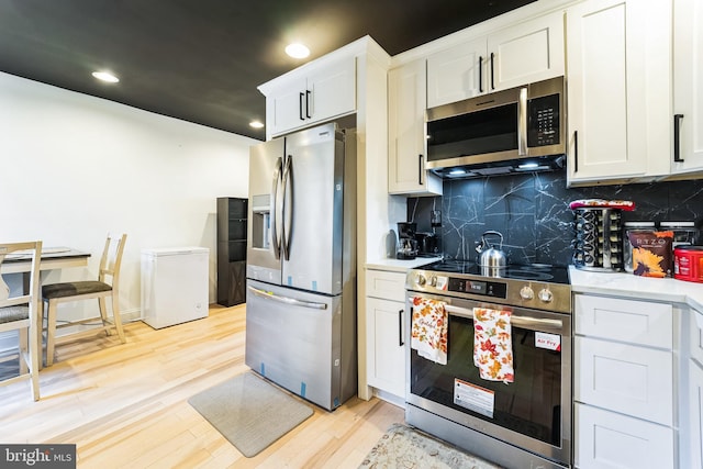 kitchen with light wood finished floors, tasteful backsplash, white cabinetry, appliances with stainless steel finishes, and light countertops