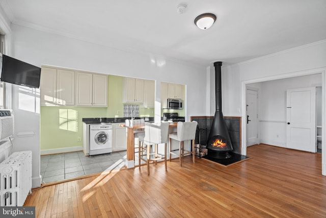 kitchen with radiator, stainless steel microwave, light wood-style floors, a wood stove, and washer / dryer