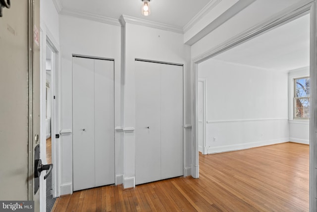 unfurnished bedroom featuring ornamental molding, two closets, hardwood / wood-style flooring, and baseboards