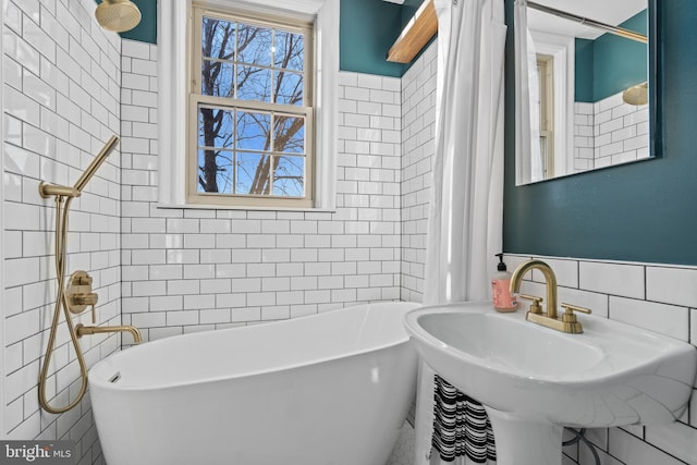 bathroom featuring curtained shower, a freestanding bath, tile walls, and a sink