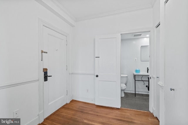 interior space with visible vents, baseboards, ensuite bath, ornamental molding, and wood finished floors