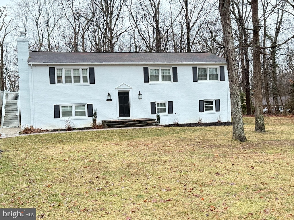 raised ranch featuring a front yard, brick siding, and a chimney