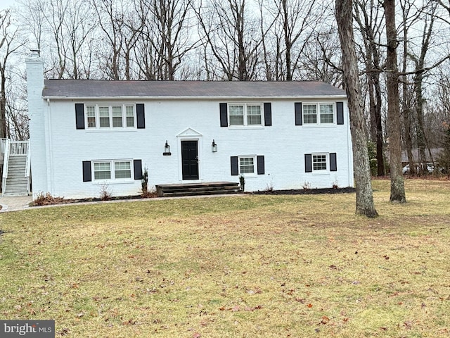 raised ranch featuring a front yard, brick siding, and a chimney