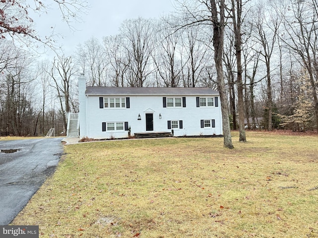 raised ranch featuring driveway, a chimney, and a front yard