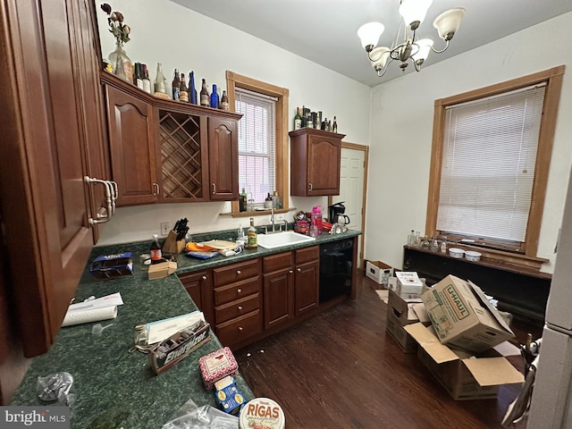 kitchen with dark countertops, dark wood finished floors, black dishwasher, an inviting chandelier, and a sink