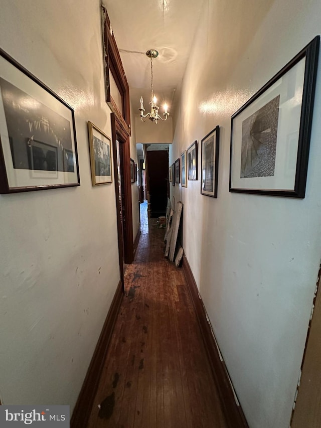 hall with baseboards, dark wood-type flooring, and an inviting chandelier