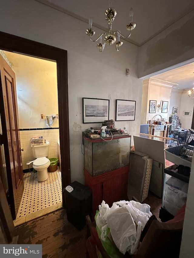 interior space with a chandelier, toilet, wainscoting, wood finished floors, and tile walls