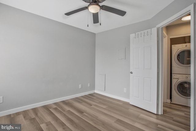 interior space with a ceiling fan, baseboards, stacked washer / dryer, and wood finished floors